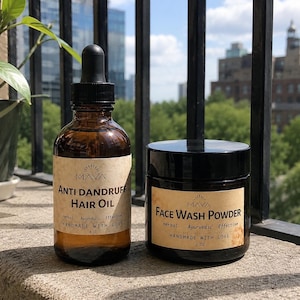 May include: An amber glass bottle of Maya Anti Dandruff Hair Oil with a black dropper cap and a 4 oz label, alongside a black jar of Maya Face Wash Powder with a 2 oz label. Both containers feature tan paper labels with black text.