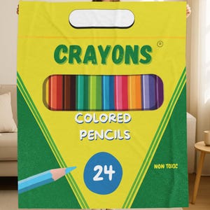 May include: A yellow and green rectangular blanket featuring a graphic design of a crayon box. The text reads CRAYONS, COLORED PENCILS, 24, and NON TOXIC. A blue pencil illustration is at the bottom left, and a row of colored pencils is in the center.