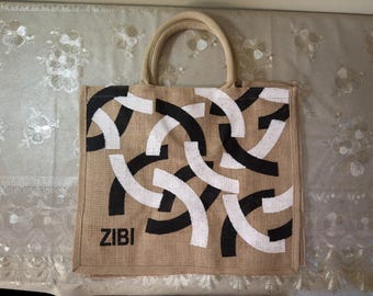 May include: A beige tote bag with a repeating pattern of black and white curved lines. The bag has two beige handles and the word "ZIBI" printed in black on the front. The bag is made of a woven material.