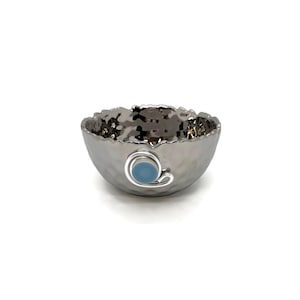 May include: A small, silver bowl with a hammered texture and a blue accent. The bowl is perfect for serving small snacks or holding jewelry.