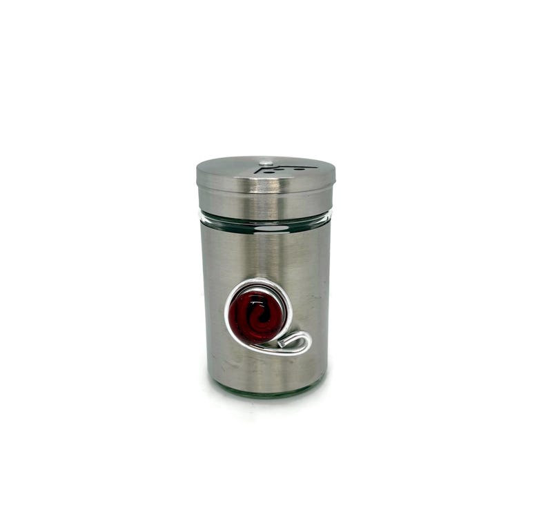 May include: A silver metal spice jar with a red glass swirl design on the side.