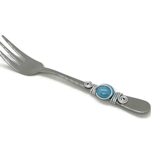 May include: A silver fork with a blue glass bead wrapped in silver wire.