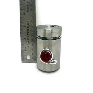 May include: A stainless steel spice jar with a glass insert and a red glass swirl accent. The jar has a screw-on lid with a small hole for dispensing spices.