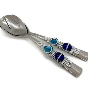 Può includere: Un paio di posate da insalata in acciaio inossidabile. I manici sono adornati con perline di vetro blu e turchese avvolte in filo d'argento. Il cucchiaio da portata ha un design a fessura.