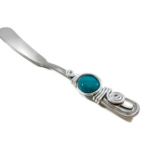 Peut inclure: Un couteau à beurre en acier inoxydable avec une perle en verre bleu sarcelle et un manche enroulé de fil argenté.