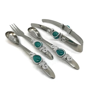 May include: A set of four silver utensils with teal blue glass accents. The set includes a fork, a spoon, a slotted spoon, and a pair of tongs.