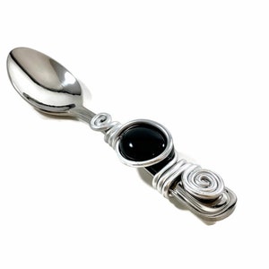 May include: A silver spoon with a black gemstone wrapped in silver wire. The handle is decorated with a silver wire spiral.
