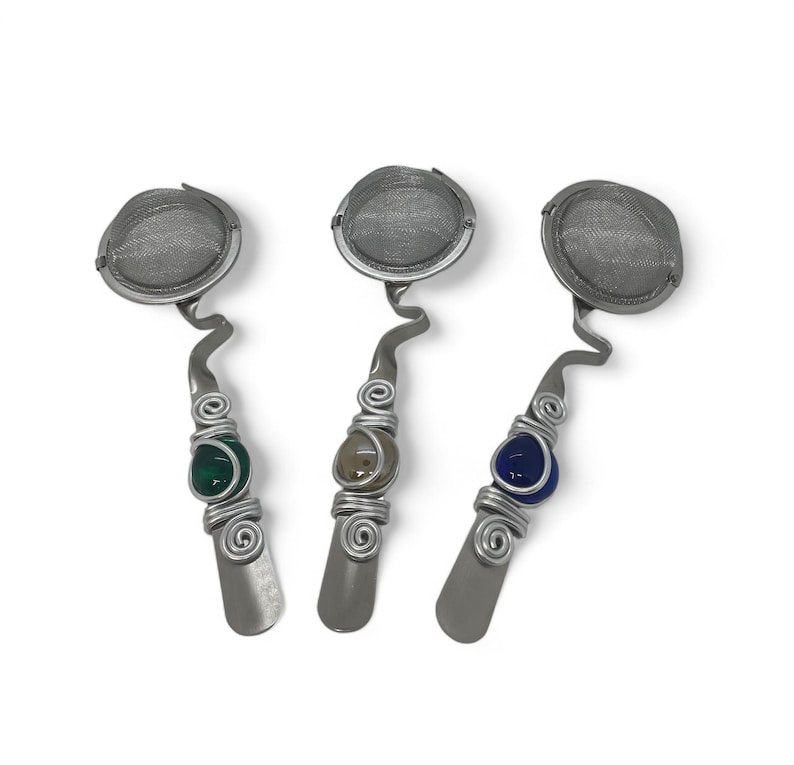 May include: Three silver tea infusers with a mesh strainer and a decorative wire wrapped handle. Each handle has a different colored glass bead: green, brown, and blue.
