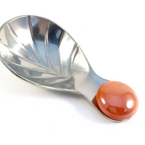 May include: A silver spoon with a fluted design and an orange plastic handle.