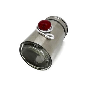 May include: A silver metal spice jar with a red glass knob on the lid.