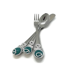 May include: A set of three silverware pieces with teal blue glass accents on the handles. The set includes a fork, a spoon, and a knife.