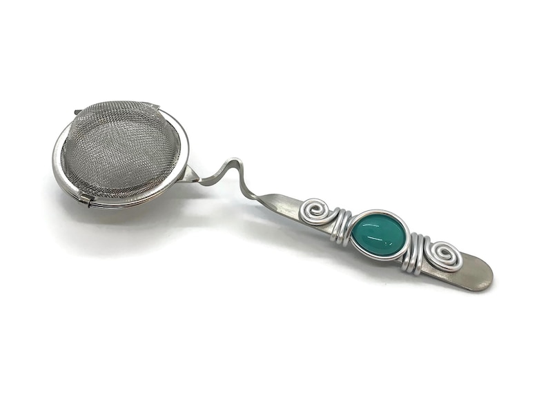 May include: A silver tea infuser with a round mesh strainer and a handle with a turquoise gemstone wrapped in wire.