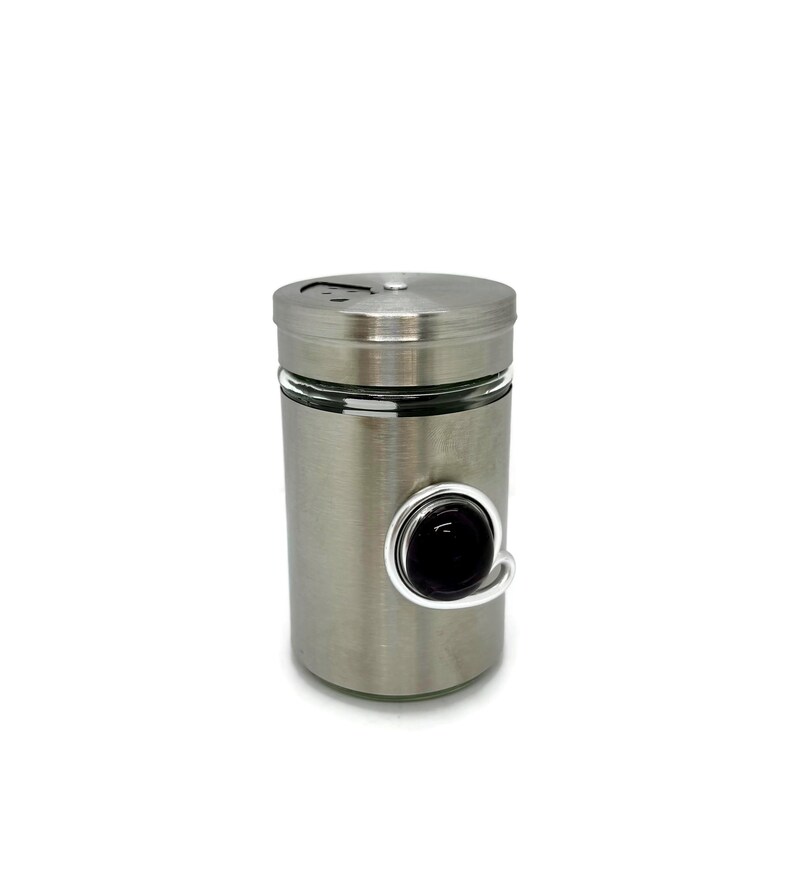 May include: A silver metal spice jar with a black glass bead on a wire loop.