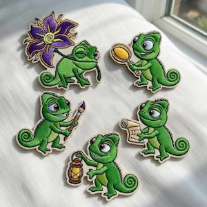 May include: Embroidered patches featuring a green chameleon in various poses. One holds a purple flower, another a magnifying glass, a paintbrush, a scroll, and a lantern. Each patch has a detailed design with a cream-colored border.