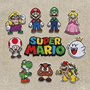 Può includere: Una collezione di nove toppe ricamate raffiguranti personaggi di Super Mario, tra cui Wario, Mario, Luigi, la Principessa Peach, Toad, un fantasma, Yoshi, un Goomba e Bowser, oltre a una toppa centrale con il testo SUPER MARIO in lettere colorate.