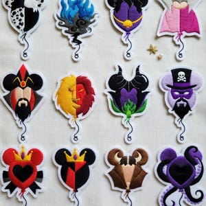 May include: A collection of embroidered patches featuring Disney villains. Each patch is shaped like a Mickey Mouse head and depicts a different character, with vibrant colors and detailed stitching. The patches include characters like Cruella, Hades, and Ursula.