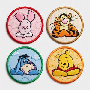 May include: Set of four embroidered patches featuring beloved characters. Includes Piglet in a pink circle, Tigger in an off-white circle, Eeyore in a blue circle, and Winnie the Pooh in an orange circle. Each patch has a colored border.