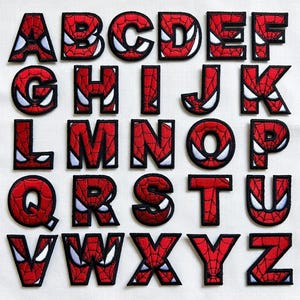 May include: A complete set of twenty-six embroidered alphabet patches from A to Z. Each letter features a red background with a black spiderweb pattern and white eye-shaped accents, all outlined in a thick black border for clear definition.