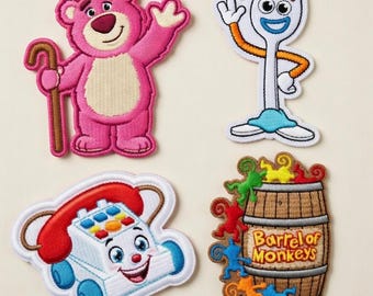 May include: Four embroidered patches featuring characters from a popular animated film. Includes a pink bear holding a cane, a white fork with orange arms, a smiling toy phone, and a barrel of monkeys with the text "Barrel of Monkeys".