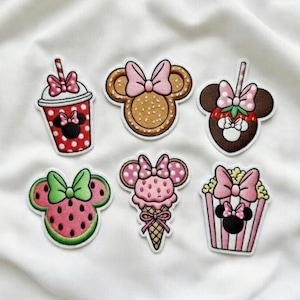 May include: A collection of six colorful embroidered patches featuring Minnie Mouse-inspired designs. The patches include a red polka-dot drink, a cookie, a strawberry, a watermelon, an ice cream cone, and a popcorn container, all with bows.