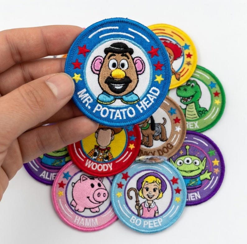 May include: A collection of embroidered patches featuring characters from the animated film Toy Story. The patches are circular, with blue, red, green, and purple borders. Characters include Mr. Potato Head, Woody, and Bo Peep.