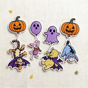 May include: A set of embroidered patches featuring cartoon characters in Halloween costumes. Tigger wears a purple cape, Piglet holds a purple balloon, Winnie the Pooh wears a purple cape, and Eeyore is attached to an orange jack-o'-lantern balloon.