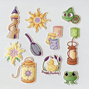 May include: A collection of embroidered patches featuring elements from a fairy tale. Includes a tower, sun, chameleon, lanterns, flower, frying pan, watering can, duck with text "The Snuggly Duckling", and a frog.
