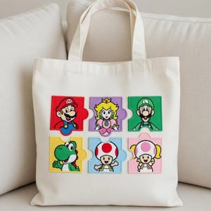 Könnte beinhalten: Beige Tragetasche mit bunten gestickten Aufnähern von Mario, Luigi, Prinzessin Peach, Yoshi, Toad und Toadette. Die Aufnäher sind in einem Puzzle-Muster angeordnet. Die Tasche hat zwei Griffe.
