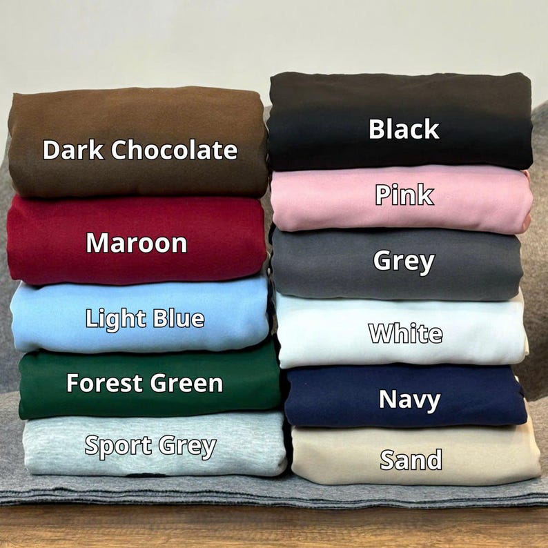 Puede incluir: Una pila de tela doblada en varios colores, incluyendo chocolate oscuro, granate, azul claro, verde bosque y gris deportivo. La pila tambi&eacute;n incluye negro, rosa, gris, blanco, azul marino y arena. Cada color est&aacute; etiquetado.