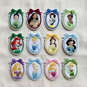 Pode incluir: Uma coleção de doze emblemas bordados ovais, cada um apresentando uma personagem feminina diferente emoldurada por uma borda colorida e um laço a condizer no topo. As personagens têm traços estilizados e cores de cabelo distintas.