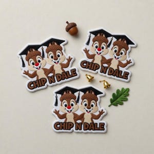 May include: Several Chip and Dale graduation patches with the text "CHIP N DALE" in brown lettering. The patches feature the cartoon chipmunks wearing graduation caps. Also included are a small acorn, two tiny gold bells, and a green leaf.