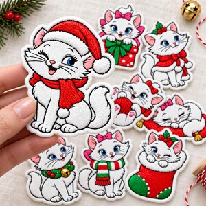 May include: A collection of embroidered patches featuring a white kitten with blue eyes in various holiday themes, including a Santa hat and scarf, a gift box, a red stocking, a wreath, and a red striped scarf, all with festive red and green accents.