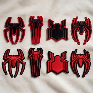 May include: Eight embroidered patches featuring various spider-inspired designs in red and black. The collection includes four distinct shapes, with two color variations for each, showcasing stylized arachnid motifs with sharp, angular lines.