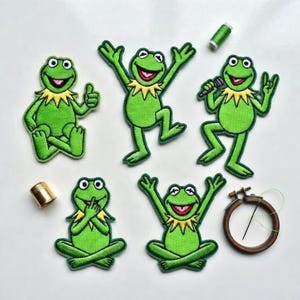 以下が含まれることがあります： 様々なポーズのカーミット・ザ・フロッグの刺繍パッチ。黄色い襟と笑顔が特徴です。付属品には、指ぬき、刺繍枠、緑色の糸が含まれています。