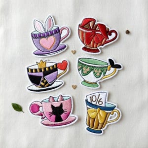 May include: Set of six embroidered patches featuring whimsical teacup designs. The patches include a purple teacup with bunny ears, a red teacup with bows, and a pink teacup with a cat silhouette. Other designs include a teacup with a crown and heart.