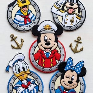May include: Embroidered patches featuring Disney characters in nautical sailor outfits. Pluto, Goofy, Mickey Mouse, Donald Duck, and Minnie Mouse are depicted in circular frames with anchors and a ship's wheel. The patches are colorful and detailed.