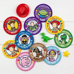 May include: A collection of colorful Toy Story character patches, including Woody, Buzz Lightyear, Jessie, and others. A small red cowboy hat, a green dinosaur, and a yellow star are also present. The patches are round with embroidered details.