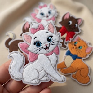 May include: Embroidered patches featuring cartoon cats in various colors. The primary patch is a white cat with a pink bow, surrounded by other cat patches in brown, orange, and white, each with a bow.