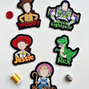 Könnte beinhalten: Gestickte Aufnäher mit Figuren aus einem beliebten Animationsfilm. Die Aufnäher zeigen Woody, Buzz Lightyear, Jessie, Rex und Bo Peep. Jeder Aufnäher hat einen schwarzen Rand und farbenfrohe Details. Ein roter Knopf, eine Garnrolle und ein Fingerhut sind ebenfalls vorhanden.