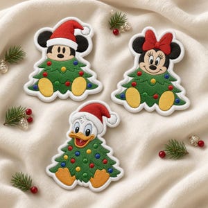 May include: Three embroidered patches featuring Mickey Mouse in a Santa hat, Minnie Mouse with a red bow, and Donald Duck in a Santa hat. Each character is depicted emerging from a green Christmas tree decorated with colorful ornaments.