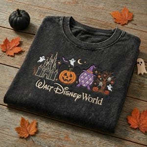Puede incluir: Una sudadera de cuello redondo gris carbón con bordados de temática de Halloween que incluyen un castillo, una calabaza, una forma geométrica morada con un sombrero de bruja y un árbol, con el texto Walt Disney World en letra blanca.