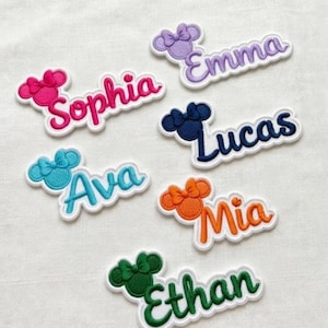Pode incluir: Patches de nomes bordados em várias cores, incluindo rosa, roxo, azul, laranja e verde. Cada patch apresenta um design de laço de orelhas de rato e um nome, como "Sophia", "Emma", "Ava", "Lucas", "Mia" e "Ethan".