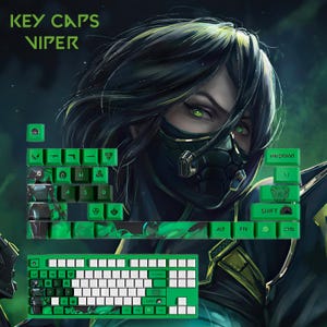 May include: Green and white keycaps with the text "KEY CAPS VIPER" and a graphic of a character with green eyes and a mask. The keycaps are designed for a keyboard and feature various symbols and letters.