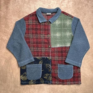 May include: A patchwork jacket with a collared neckline and button closure. The jacket features a mix of textures and patterns, including plaid, solid blue, and a leaf print. Two pockets are visible on the front. The sleeves and collar are a solid blue color.