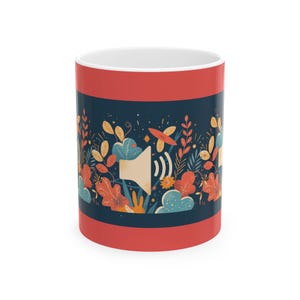 May include: A white ceramic mug with a red top and bottom band. The mug features a dark blue band with a colorful floral design and a speaker icon. The design includes leaves, flowers, and cloud shapes in shades of orange, yellow, and blue.