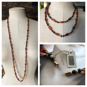 May include: A long, brown and black beaded necklace with a gold clasp. The necklace is made of faceted, teardrop-shaped beads and is double-stranded. The necklace has a tag that says "AVON".
