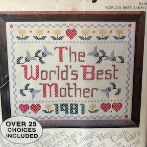 May include: A cross stitch pattern with a white background and red, green, and yellow embroidery. The pattern reads "The World's Best Mother 1981". The pattern includes over 25 choices for different titles, including mother, father, aunt, teacher, and more.