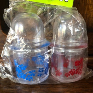 May include: Two clear plastic containers with blue and red floral designs. The containers are packaged together in a clear plastic bag. The bag has a label that reads "Made in Hong Kong".