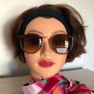 May include: Brown tortoise shell round sunglasses with gold accents and brown tinted lenses. The sunglasses have a "UV Protection" label on the right lens.