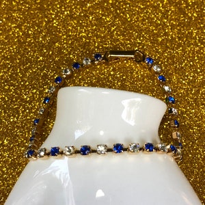 May include: A gold chain bracelet with alternating blue and clear rhinestones.